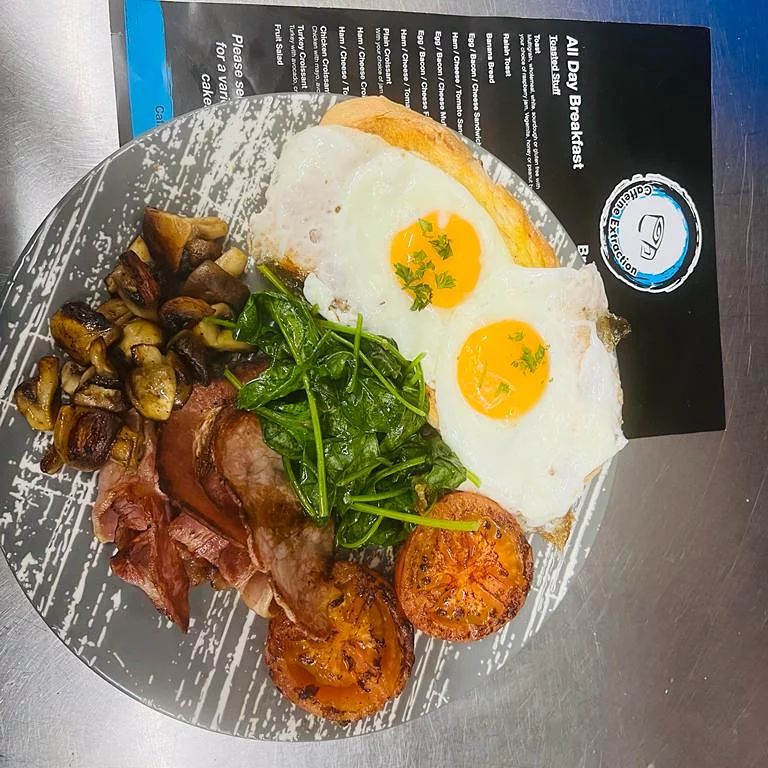A big breakfast plate with eggs, ham, mushrooms, wilted spinach, grilled tomato and toast